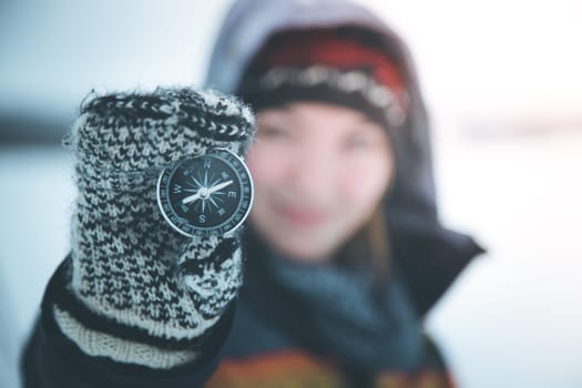 Young smiling woman holds up a compass. Wintertime, gloves and hood.