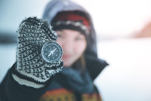 Young smiling woman holds up a compass. Wintertime, gloves and hood.