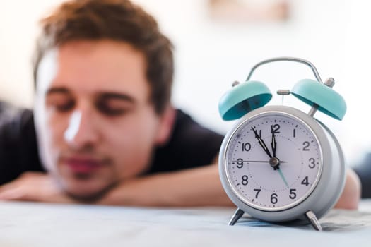 White alarm clock in the morning. Young man sleeps in the background.