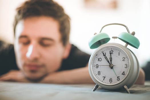White alarm clock in the morning. Young man sleeps in the background.