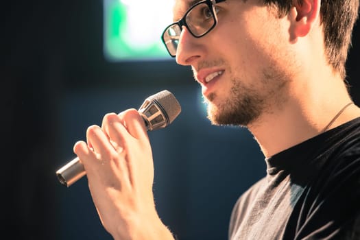 Young man on the stage is talking into a microphone, speech