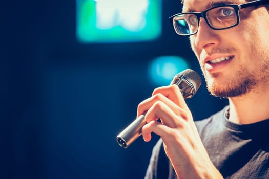 Young man on the stage is talking into a microphone, speech