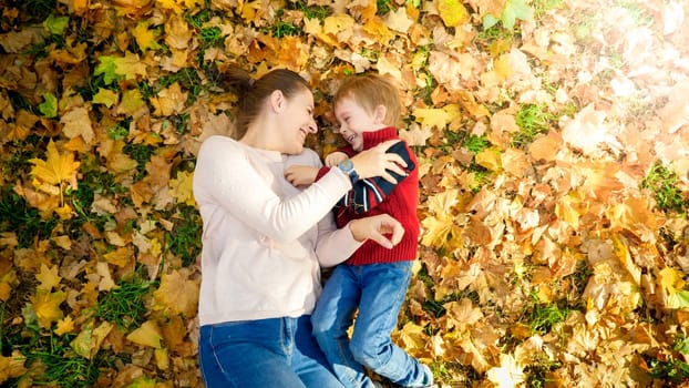 Happy smiling and laughing family lying on ground covered with yellow fallen autumn leaves at park.