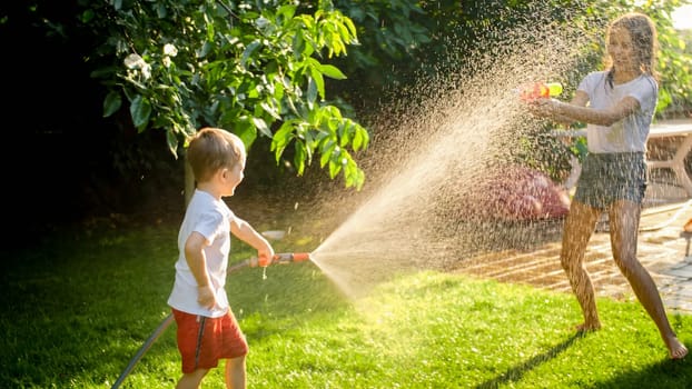 Litle boy having water fight on the backyard with his sister.