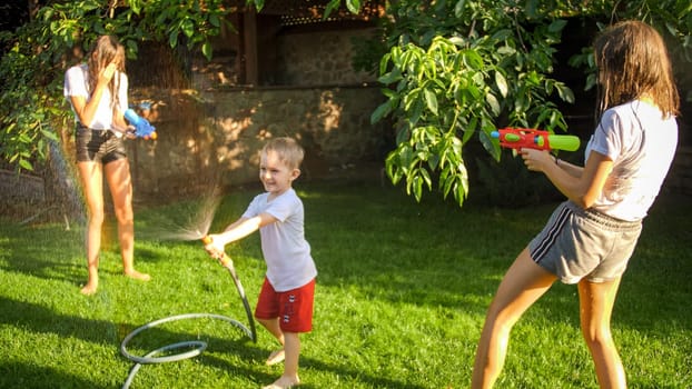 Happy laughing children playing with garden water hose at garden.