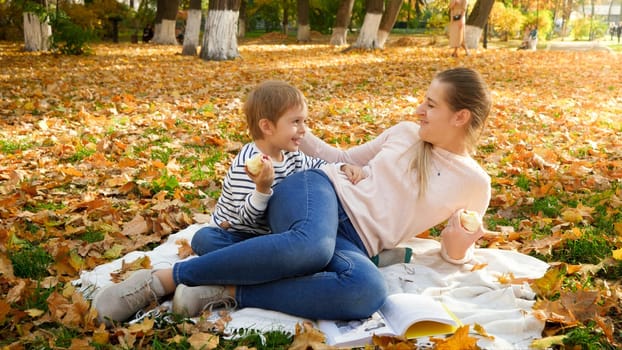 Happy young woman with her little son lying on blanket at autumn park and smiling at each other.