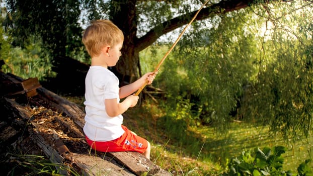 Portrait of cute little boy catching fish at old pond in country.