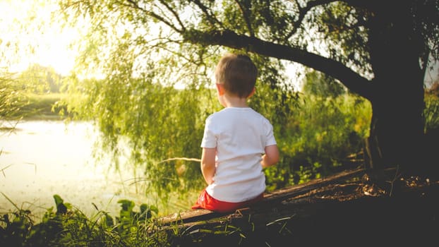 Toned rear view photo of little boy fishing on the river at sunset.