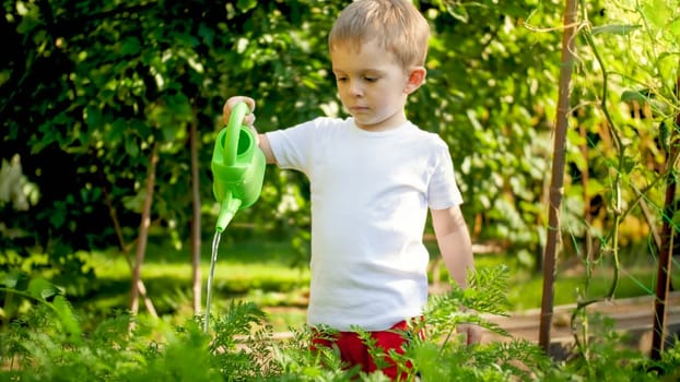 Portrait of cute little boy with watering can in garden.