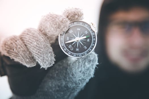 Young smiling man holds up a compass. Wintertime, gloves and hood.