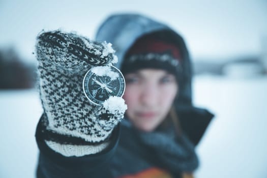 Young woman holds up a compass. Wintertime, gloves and hood.