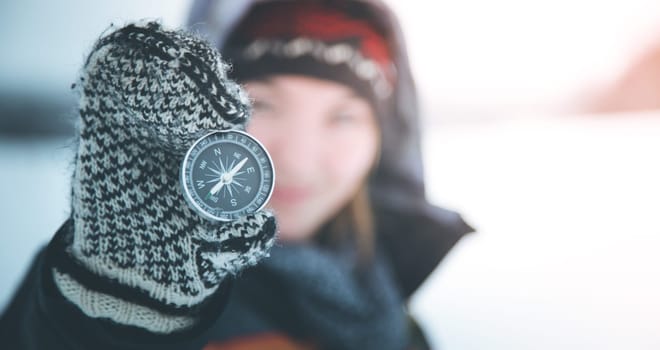 Young smiling woman holds up a compass. Wintertime, gloves and hood.