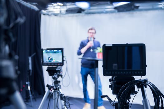 Male journalist in a television studio talks into a microphone, film cameras