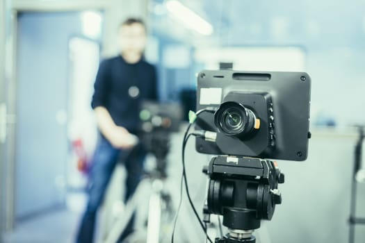 Lens of a film camera in an television broadcasting studio, spotlights and equipment, cameraman in the blurry background