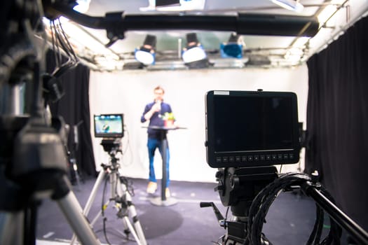 Male journalist in a television studio talks into a microphone, film cameras