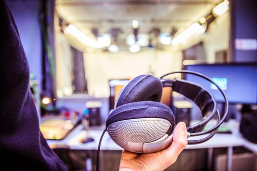 Young man holds headphones in the recording studio. Buttons, studio, screens and equipment in the blurry background