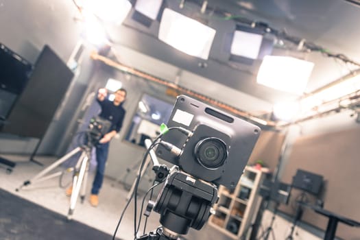 Lens of a film camera in an television broadcasting studio, spotlights and equipment, cameraman in the blurry background