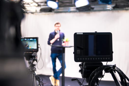 Male journalist in a television studio talks into a microphone, film cameras