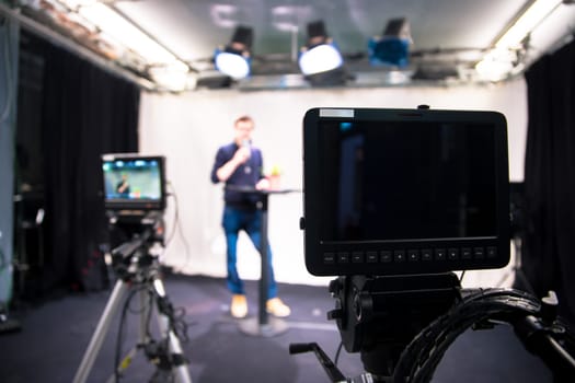 Male journalist in a television studio talks into a microphone, film cameras