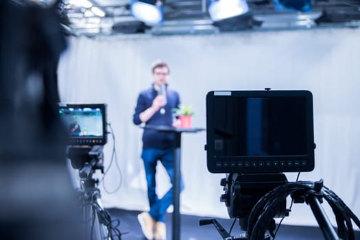 Male journalist in a television studio talks into a microphone, film cameras
