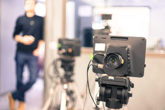 Lens of a film camera in an television broadcasting studio, spotlights and equipment, director in the background