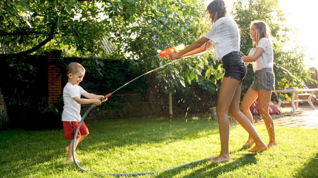 Happy laughing children having water gun fight on hot sunny summer day.