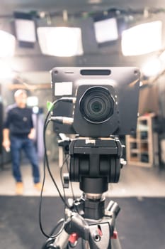 Lens of a film camera in an television broadcasting studio, spotlights and equipment, director in the background