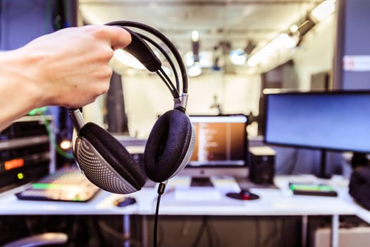 Young man holds headphones in the recording studio. Buttons, studio, screens and equipment in the blurry background