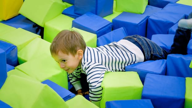 Portrait of active little boy having fun and playing in soft pit at playroom in shopping mall.