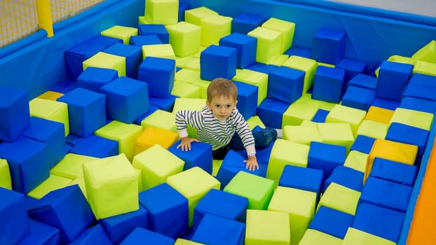 Cute little boy playing in pool full of soft cubes in palyroom.