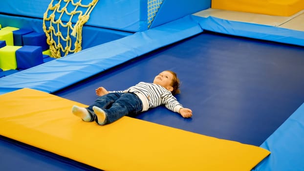 Cute little tired boy lying on trampoline after palying and jumping at playground.