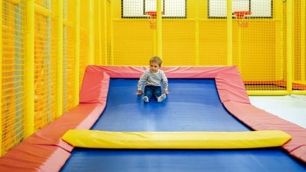 Cute little boy sliding and jumping on tramploines at playroom in shopping mall.