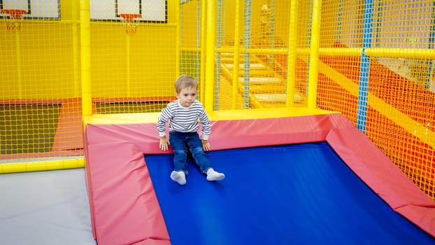 Cute little boy sliding down on the slide in playroom at shopping mall.