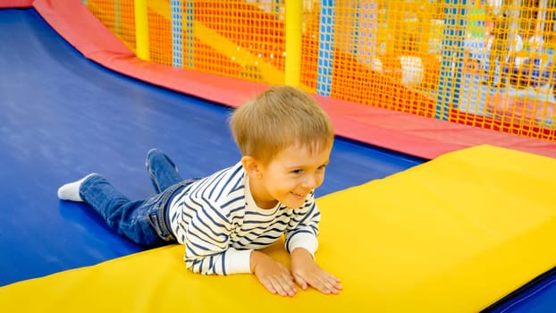 Portrait of happy laughing little boy lying on tramploine at amusement park.