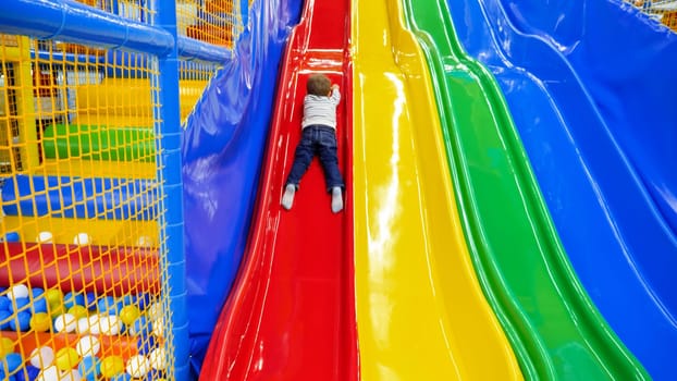 Little toddler boy sliding on colorful slide in ausement park at shopping mall.