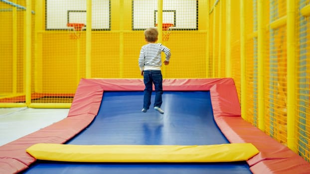 Rear view photo of little boy jumping and having fun on trampoline at amusement park.