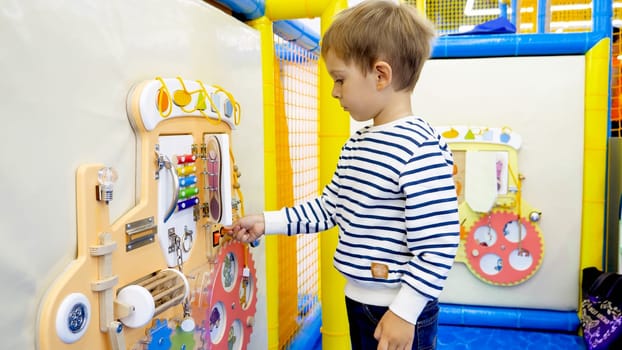 Cute little boy playing with buttons and knobs on educational child's board in kindergarten.