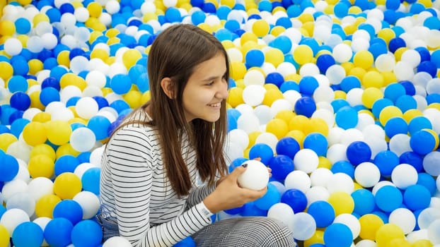 Portrait of smiling teenage girl fell in pit with soft colorful balls on playground at shopping mall.