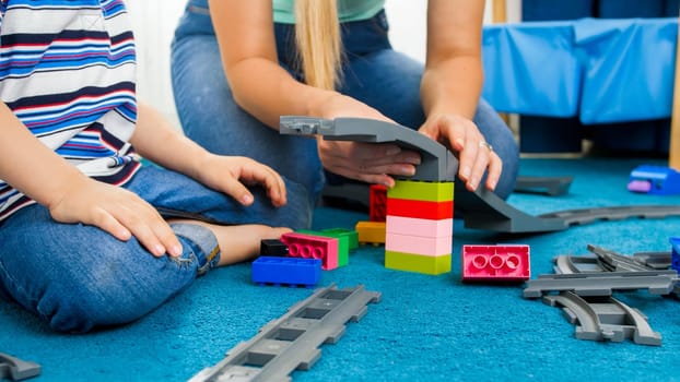 Closeup image of mother with little son playing with toy railroad on floor.