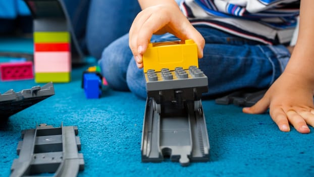 Closeup photo of little toddler boy playing woth toy train and railroad on carpet at playroom.