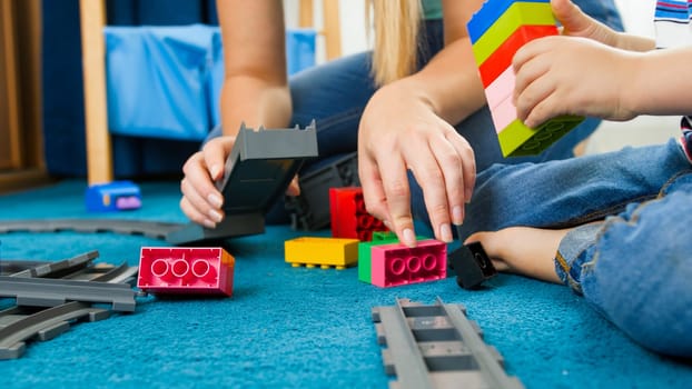 Closeup image of young caring mother helping her son building toy railroad.