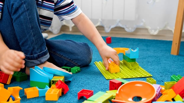 Closeup image of little boy assembling colorful toy constructor on carpet.
