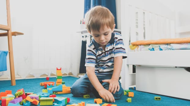 Toned photo of little smiling boy playing with constructor blocks in his bedroom.