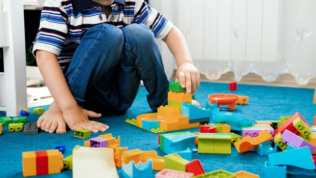 Closeup image of little boy building a house with colorful constructor blocks.
