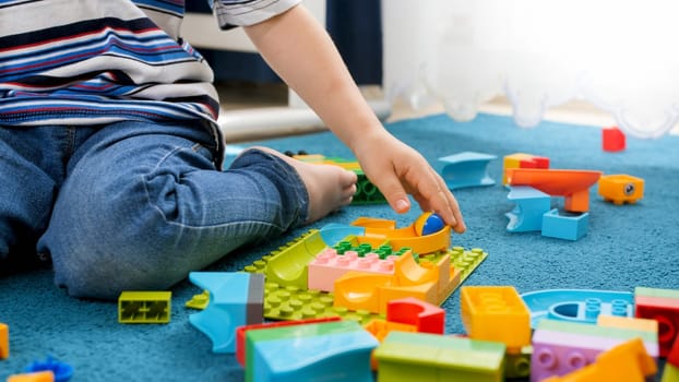 Closeup image of little toddler boy assembling track for marble run game.