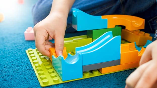 Closeup image of boys hand building toy track using constructor blocks.
