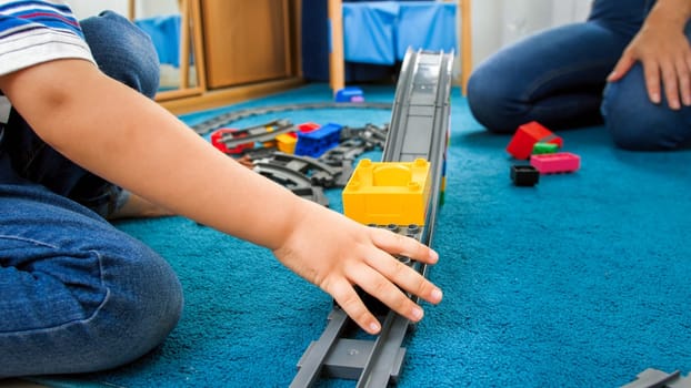 Closeup image of child's hand palying with toy train and railroad on floor.