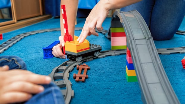 Young mother with her little playing a game with trains and railroad on floor.