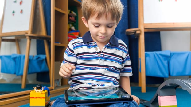 Portrait of happy smiling little boy watching cartoons on digital tablet computer in his room.