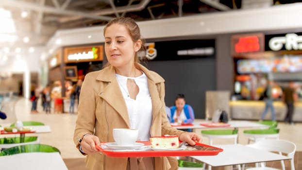 Portrait of young girl holding food on tray looking for place to eat on food court at shopping mall.